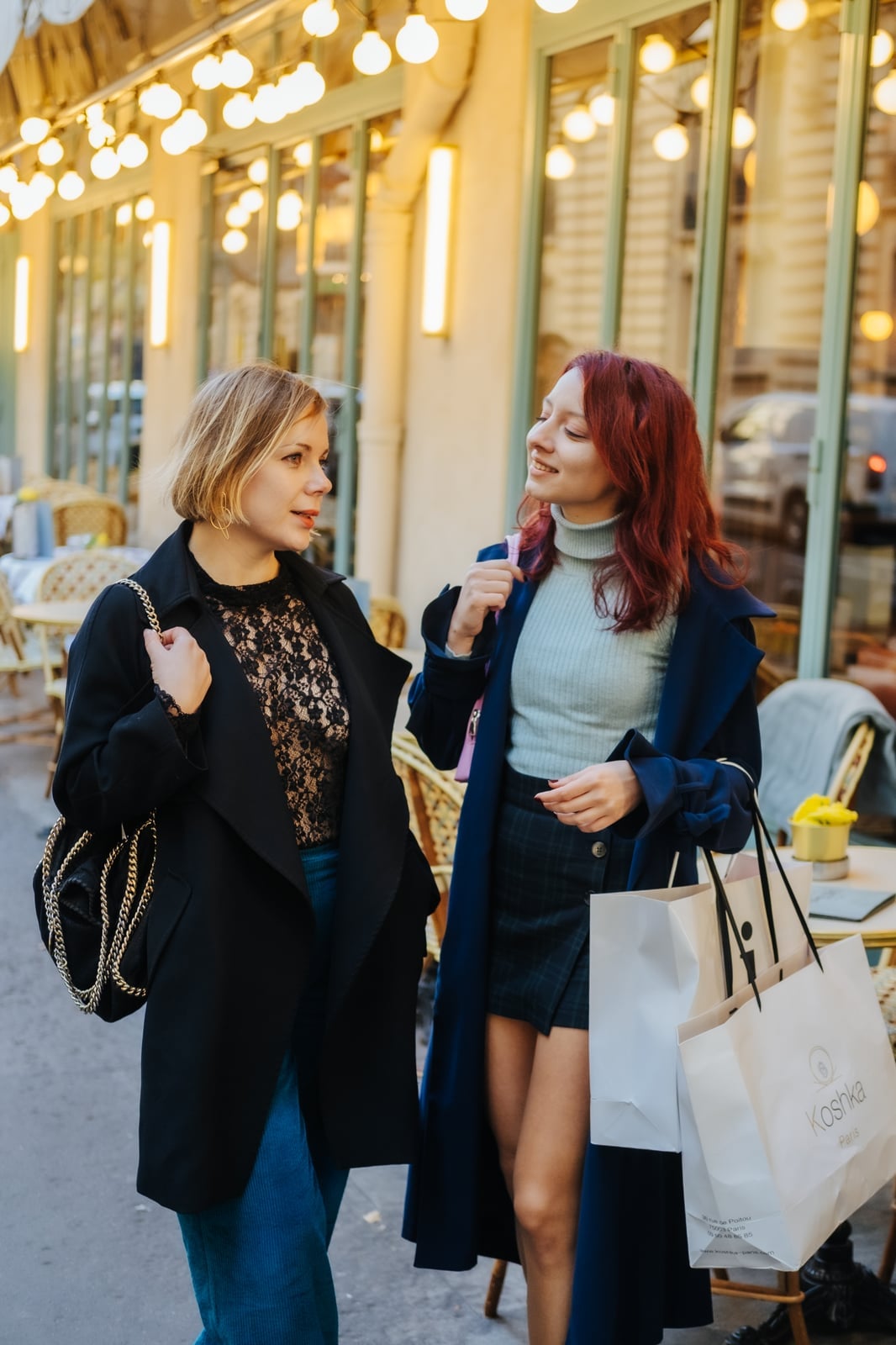 Two women dressed in autumn layers walking through a Parisian boutique street